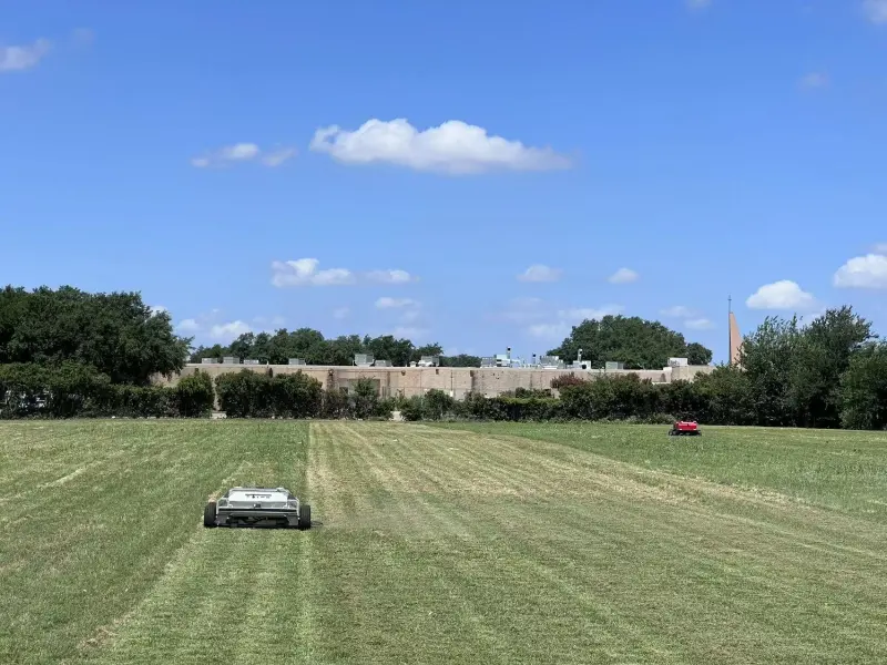 Two autonomous mowers cutting a large campus lawn